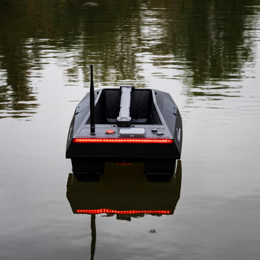 Modern carbon fiber GPS bait boat with red LED lights and sonar system floating on water, perfect for carp fishing and precision bait delivery