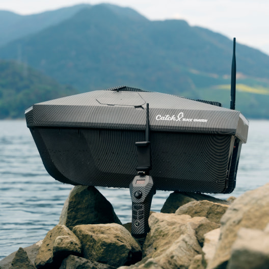 Advanced GPS bait boat with fish finder and sonar antenna mounted on rocky shoreline showcasing modern fishing technology