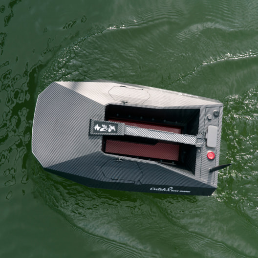 carbon fiber GPS bait boat with dual hopper floating on water, equipped with fish finder and remote control capabilities