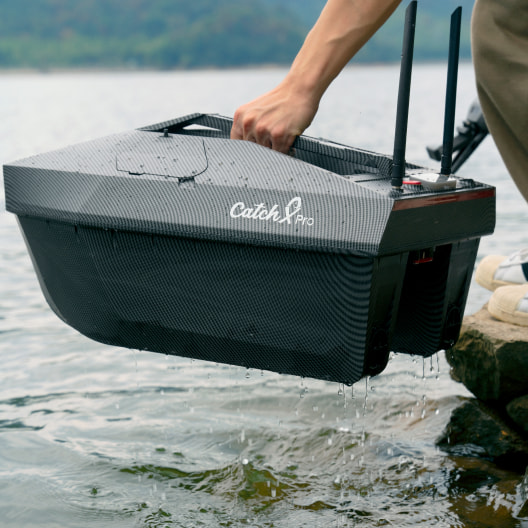 Professional GPS bait boat with dual hopper being lowered into lake water, featuring Catch Pro design and waterproof housing