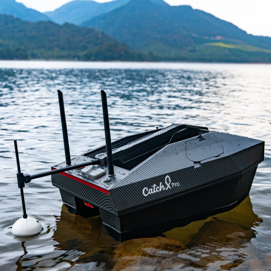 Advanced GPS bait boat CatchX Pro with dual hopper floating on mountain lake, featuring carbon fiber design and sonar capabilities