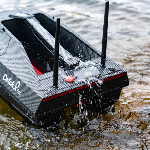 GPS bait boat with fish finder splashing through water, featuring dual hopper and carbon-fiber design with red accents