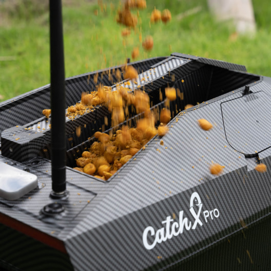 Bait boat dispensing bait, labeled CatchX Pro, ideal for carp fishing with GPS and fish finder features