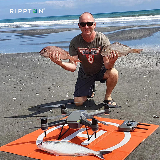 Man showcasing freshly caught fish with SharkX fishing drone with bait release on a beach, highlighting waterproof features